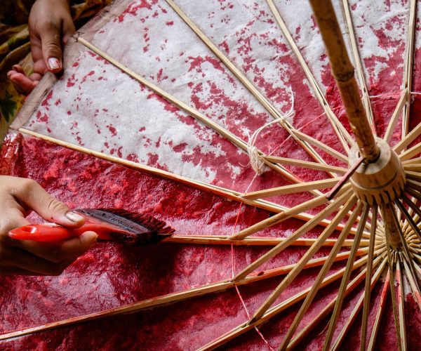 Asian woman hands painting a paper and bamboo umbrella with red color